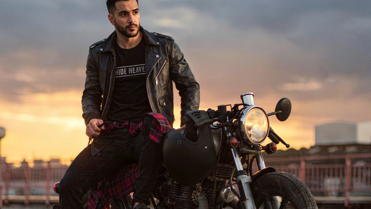 Man sitting on a motorcycle with a sunset wearing leather jacket
